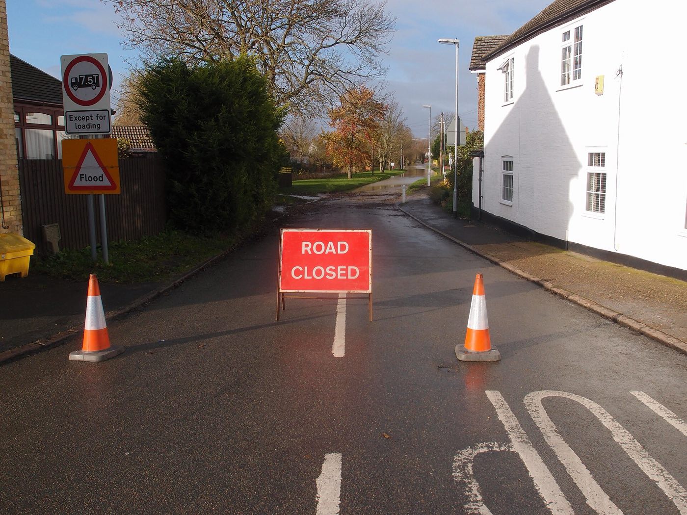 A road closed sign and flood warning triangle on a flooded village road in England